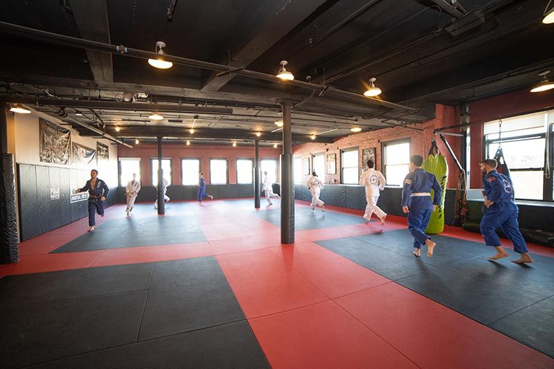 Martial arts class training on red mats in a mirrored studio with heavy bags and large windows