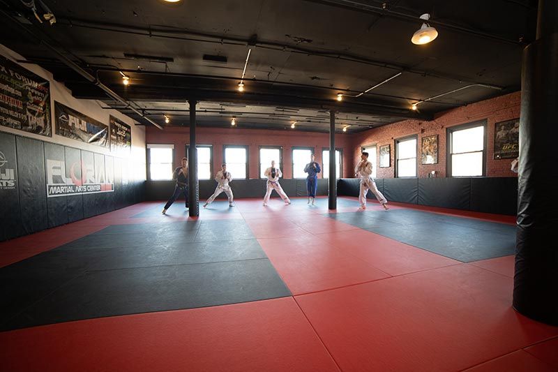 Martial arts studio with red-and-black mats and several people practicing in the center
