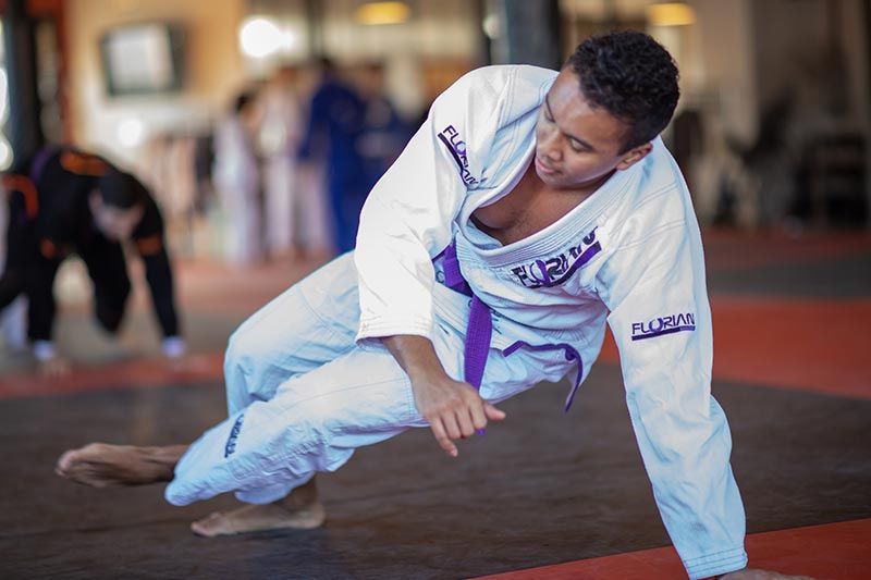 Person practicing a martial arts ground move on a mat in a white gi.