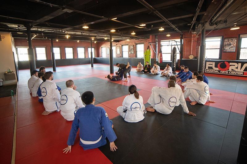 Martial arts class seated in a gym, with a coach in the center and students in white gis around them