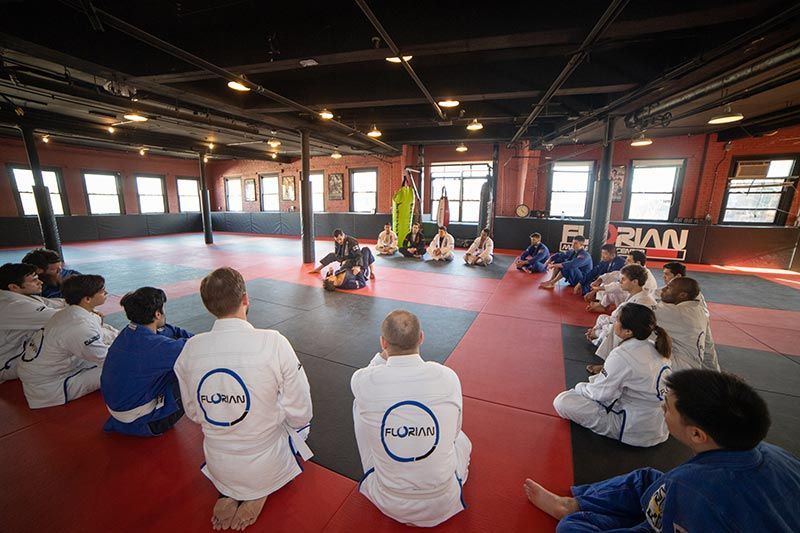 Martial arts class seated in a circle on red mats inside a bright training studio
