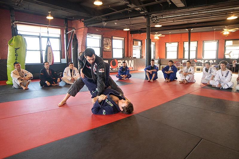 Martial arts class practicing grappling on red mats in a bright gym studio