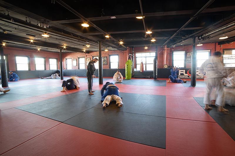 Mats in a martial arts studio with people training and grappling on the floor