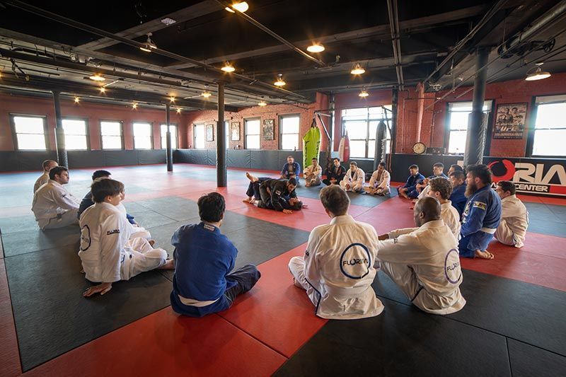 Martial arts class seated in a circle on red mats inside a gymnasium