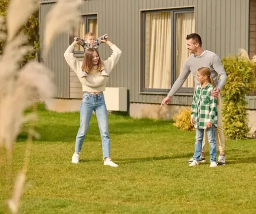 Family playing in a grassy yard outside a house, with a child and two adults smiling.