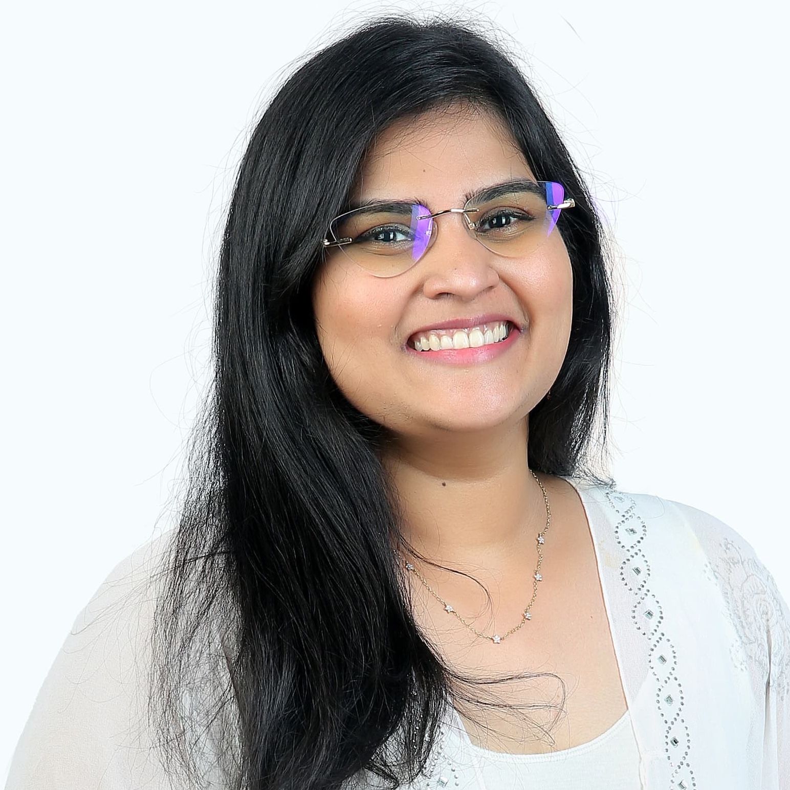 Woman with dark hair and glasses smiles, wearing a light-colored top, set against a white backdrop.