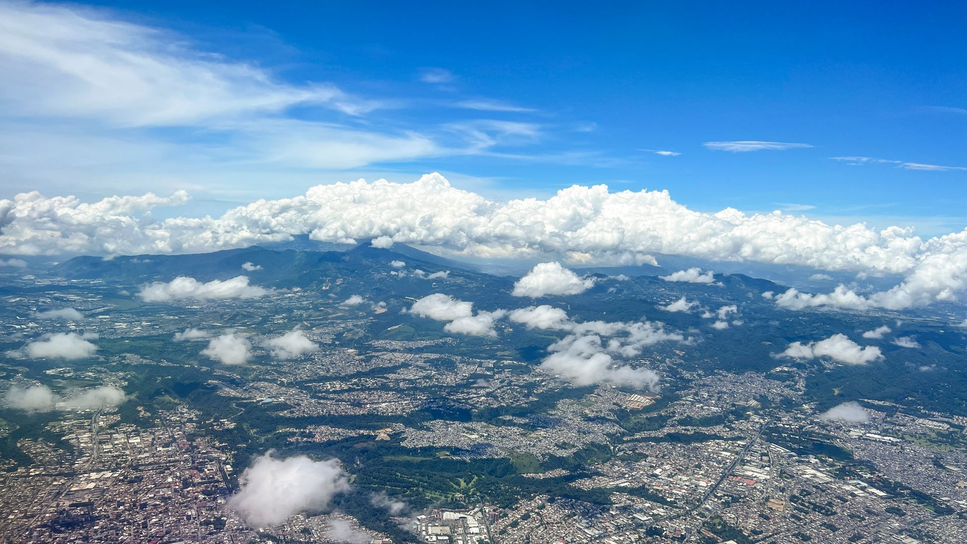 Cityscape with mountains, partly obscured by clouds, under a bright blue sky.