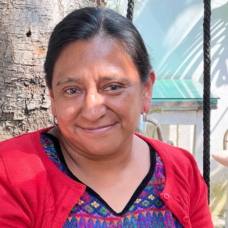 Woman in red sweater smiles outdoors, wearing patterned shirt.