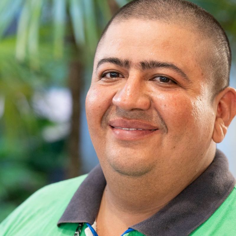 Smiling man with short dark hair, wearing a green shirt with a gray collar, outside.