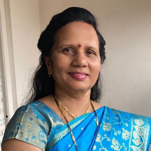 Woman with dark hair, wearing a blue sari and gold jewelry, smiling.