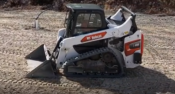 White Bobcat skid-steer loader with bucket on dirt ground, side view