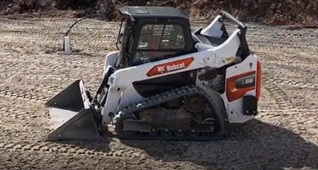 White Bobcat skid-steer loader with bucket on dirt ground, side view