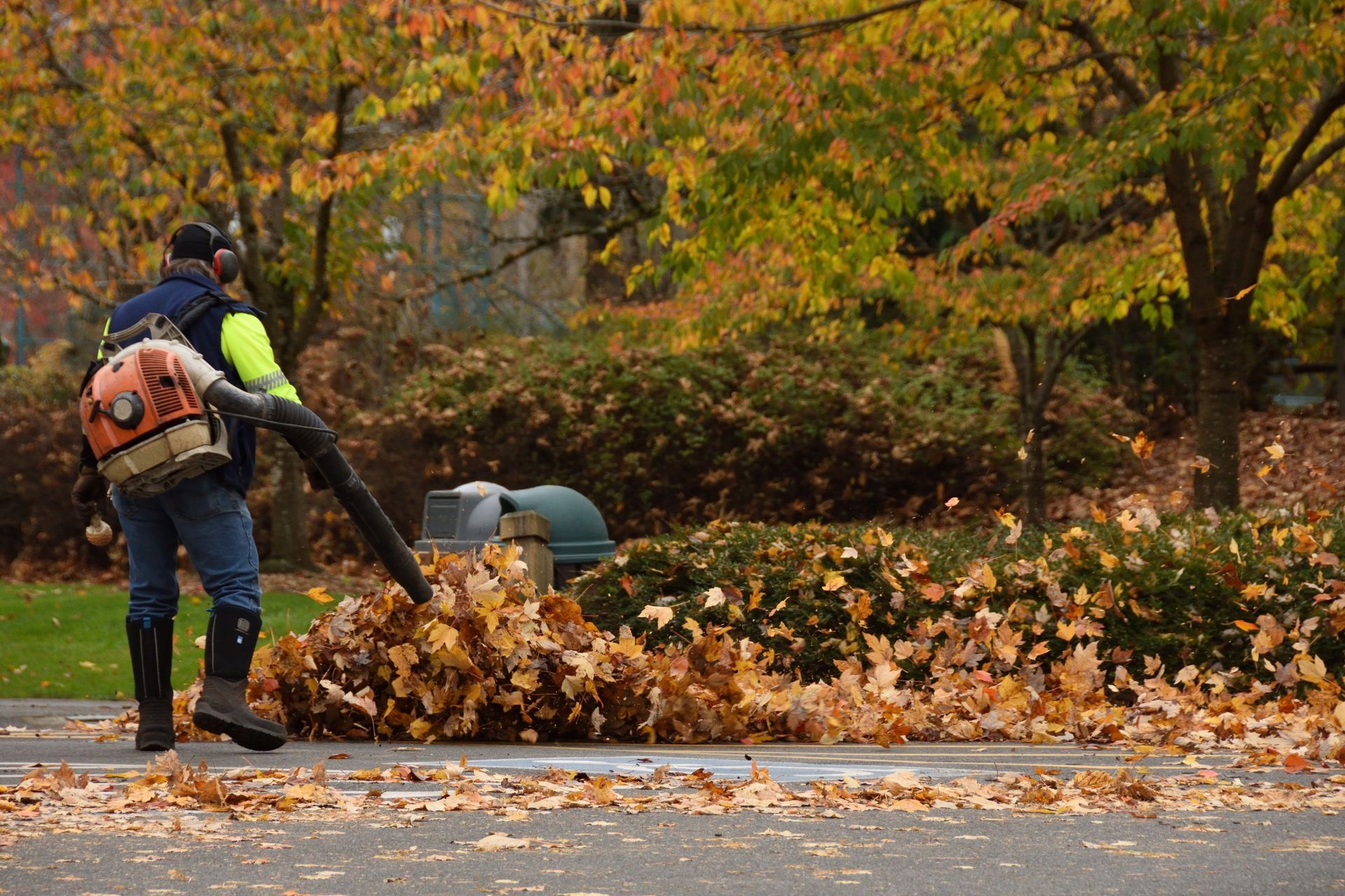 Worker using a leaf blower to clear autumn leaves on a street