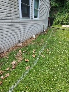 House siding with a narrow dirt trench along the lawn and scattered leaves; garden hose near the side yard