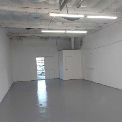 An empty room with white walls, a gray shiny floor, and bright ceiling lights. 