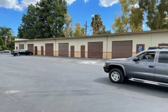 A row of storage units with brown doors sits in front of an open parking area