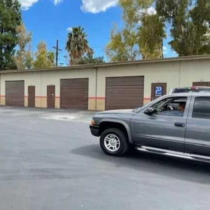 A row of storage units with brown doors sits in front of an open parking area