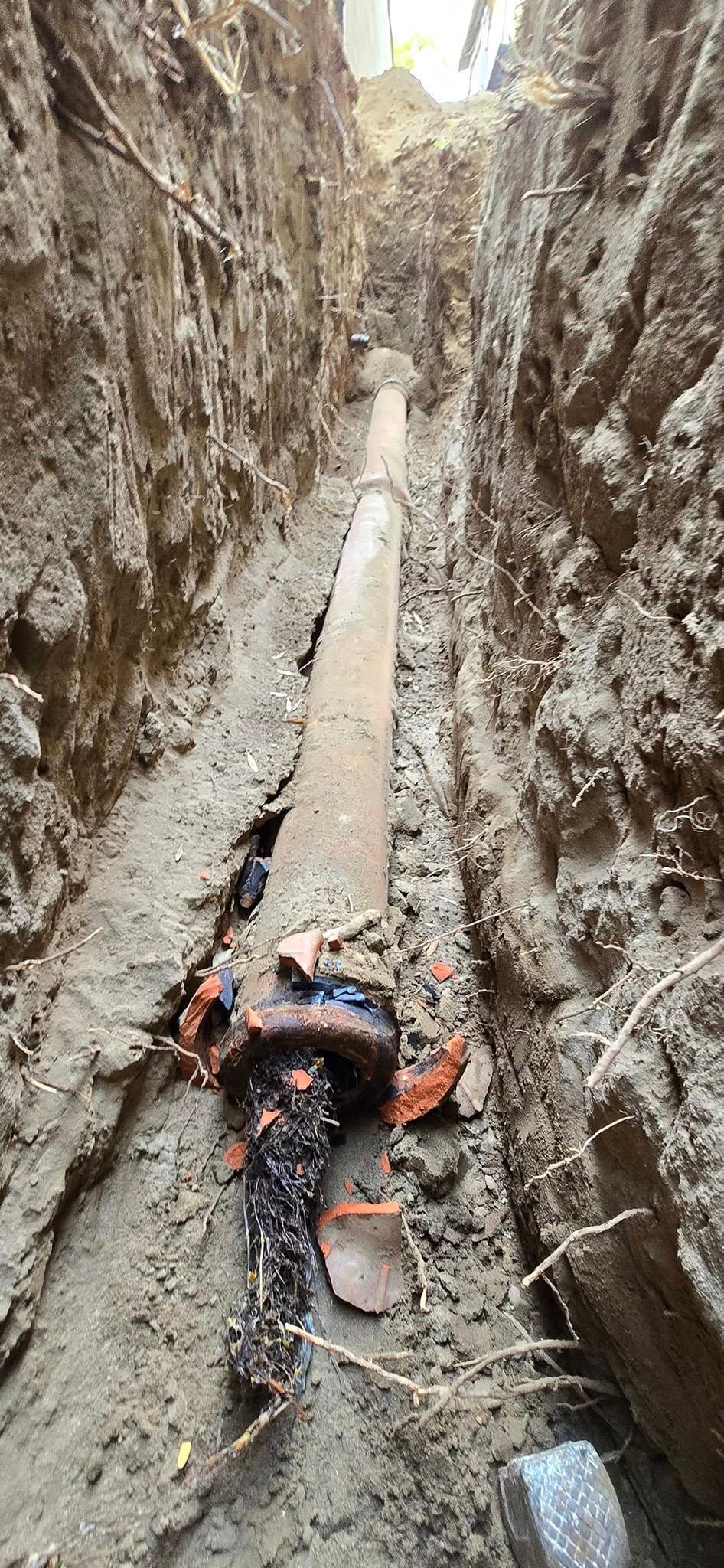 A large pipe is laying in the dirt in a trench.
