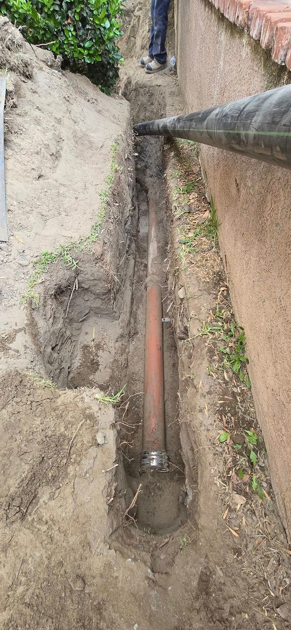 A man is digging a hole in the ground next to a wall.