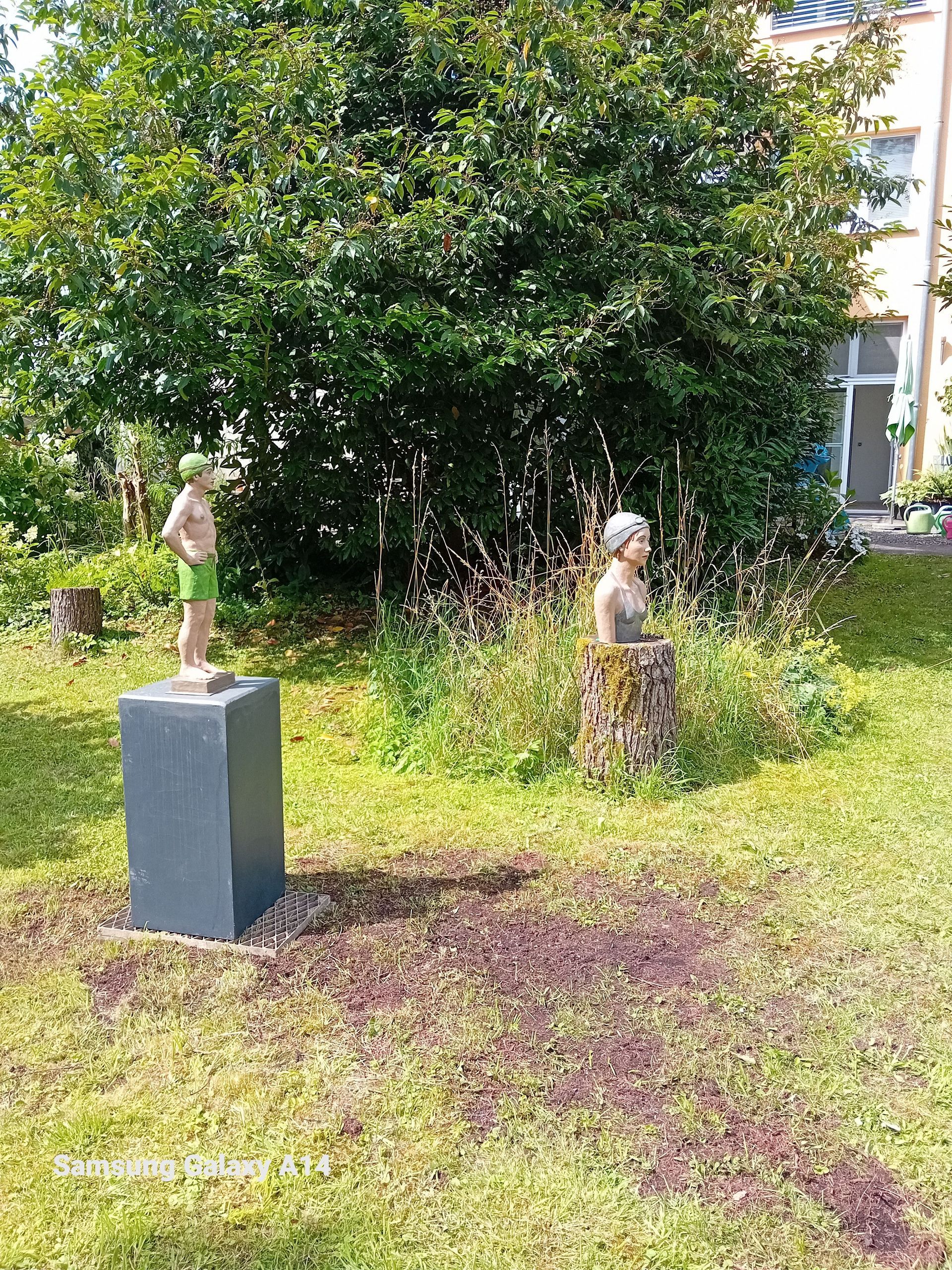 Ein paar Statuen, die nebeneinander auf einer Wiese stehen.