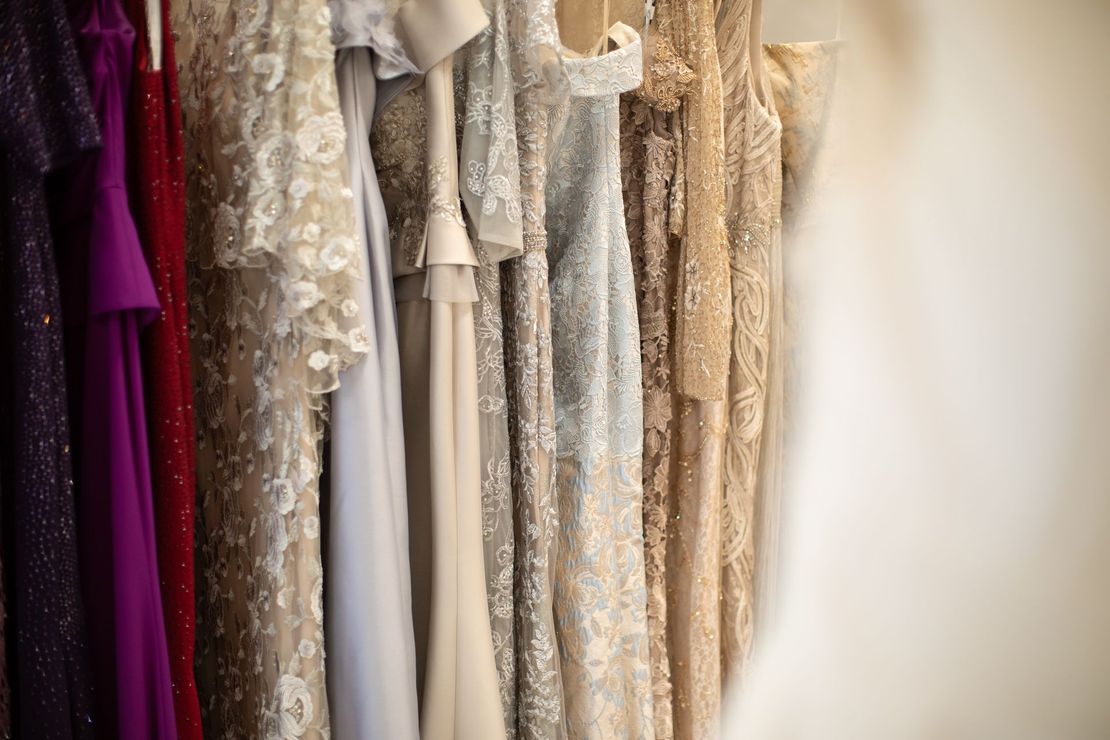 Row of formal gowns in various colors and textures hanging on a rack.