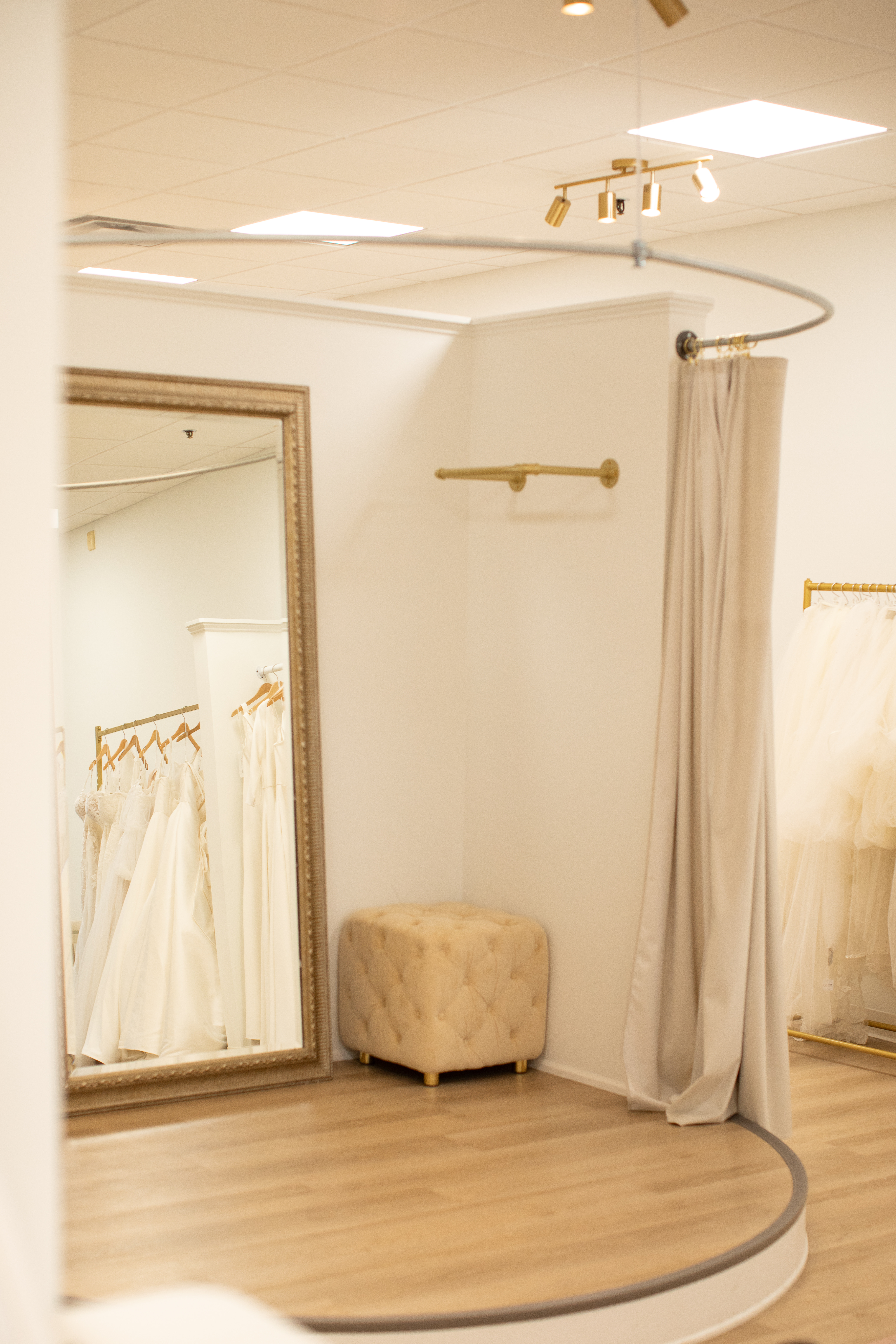 Ivory-colored wedding dresses hang on wooden hangers, tagged