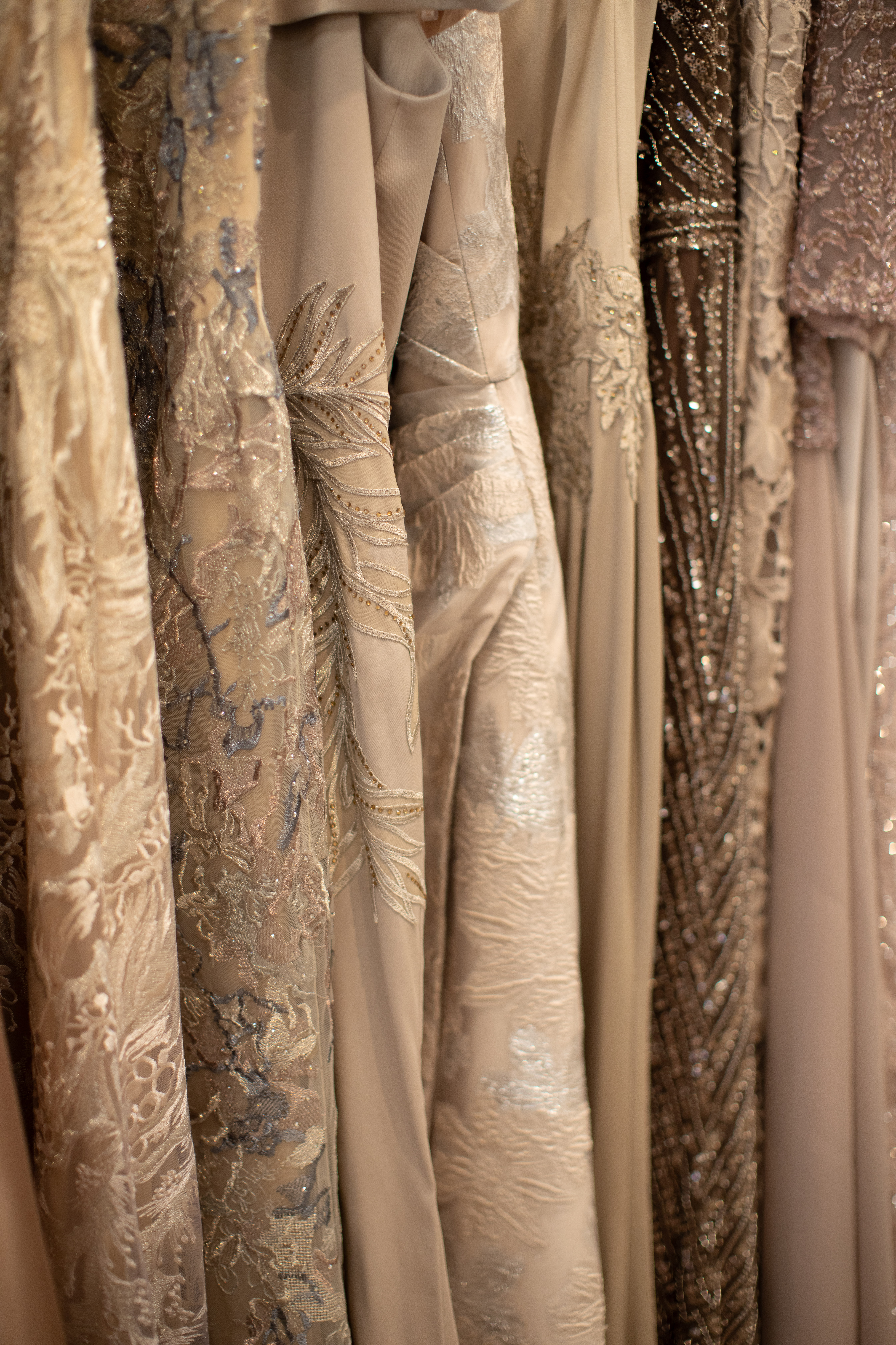 Row of sequined and solid-colored formal dresses hanging in a boutique, varying shades of beige, gray, and brown.