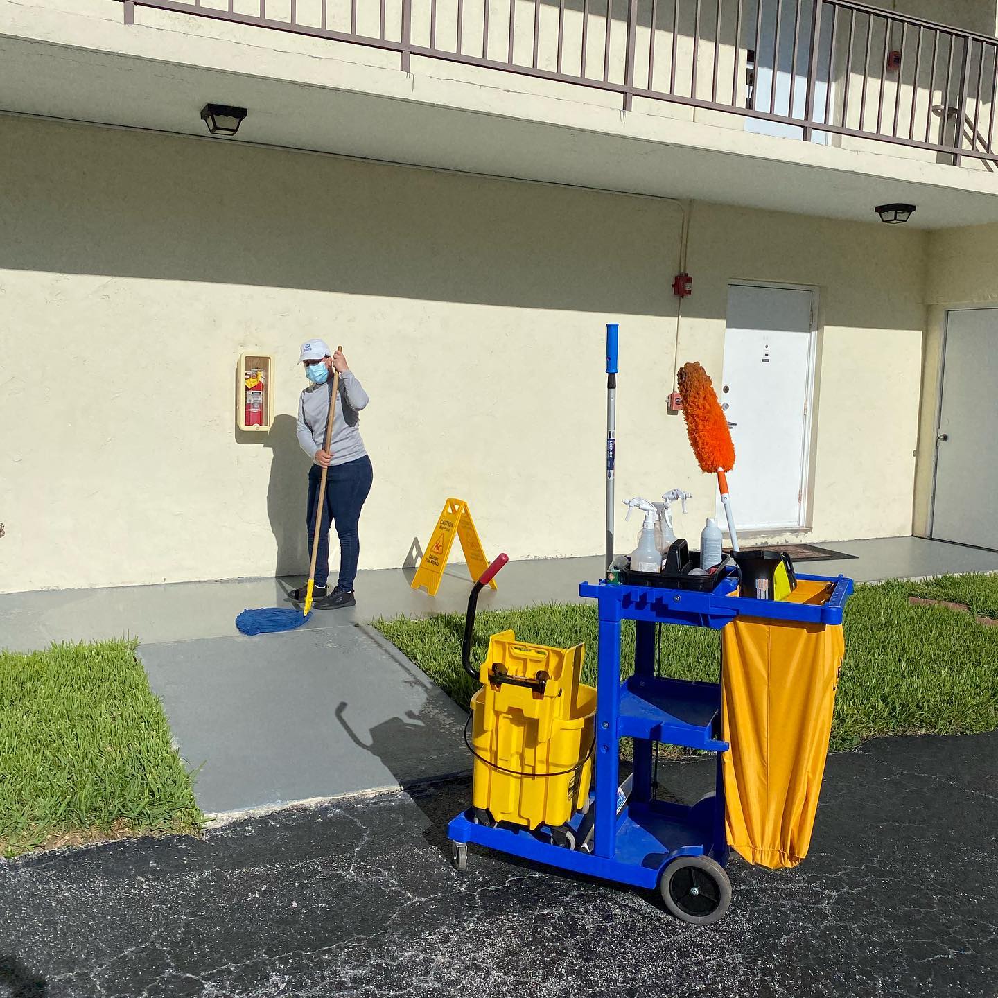 A woman is mopping the sidewalk in front of a building