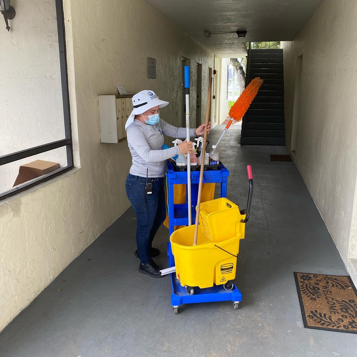 A woman wearing a mask is cleaning a hallway with a mop and buckets.