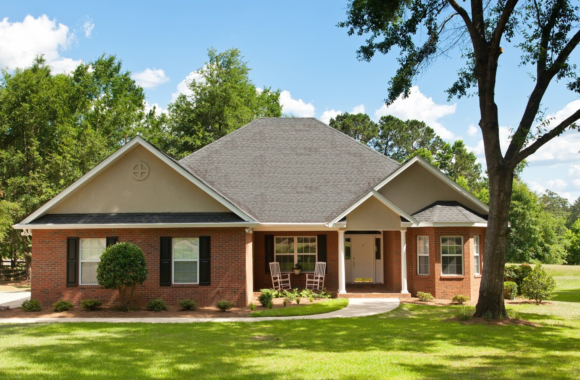 Brick house with black shutters, green lawn, and blue sky.