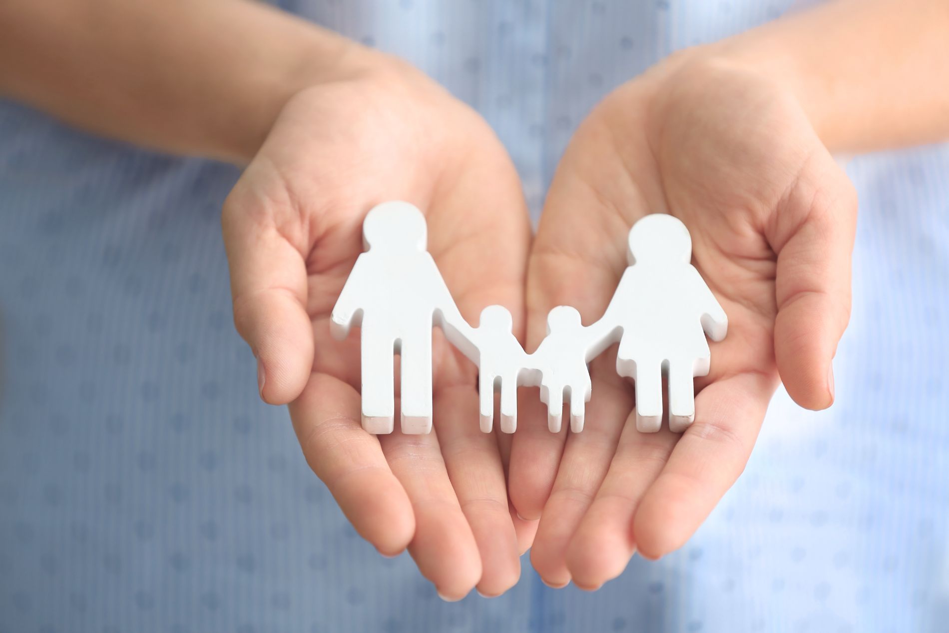 Hands holding a white family figurine, symbolizing care and protection.