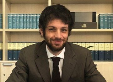 Un uomo in giacca e cravatta è seduto a una scrivania davanti a una libreria.