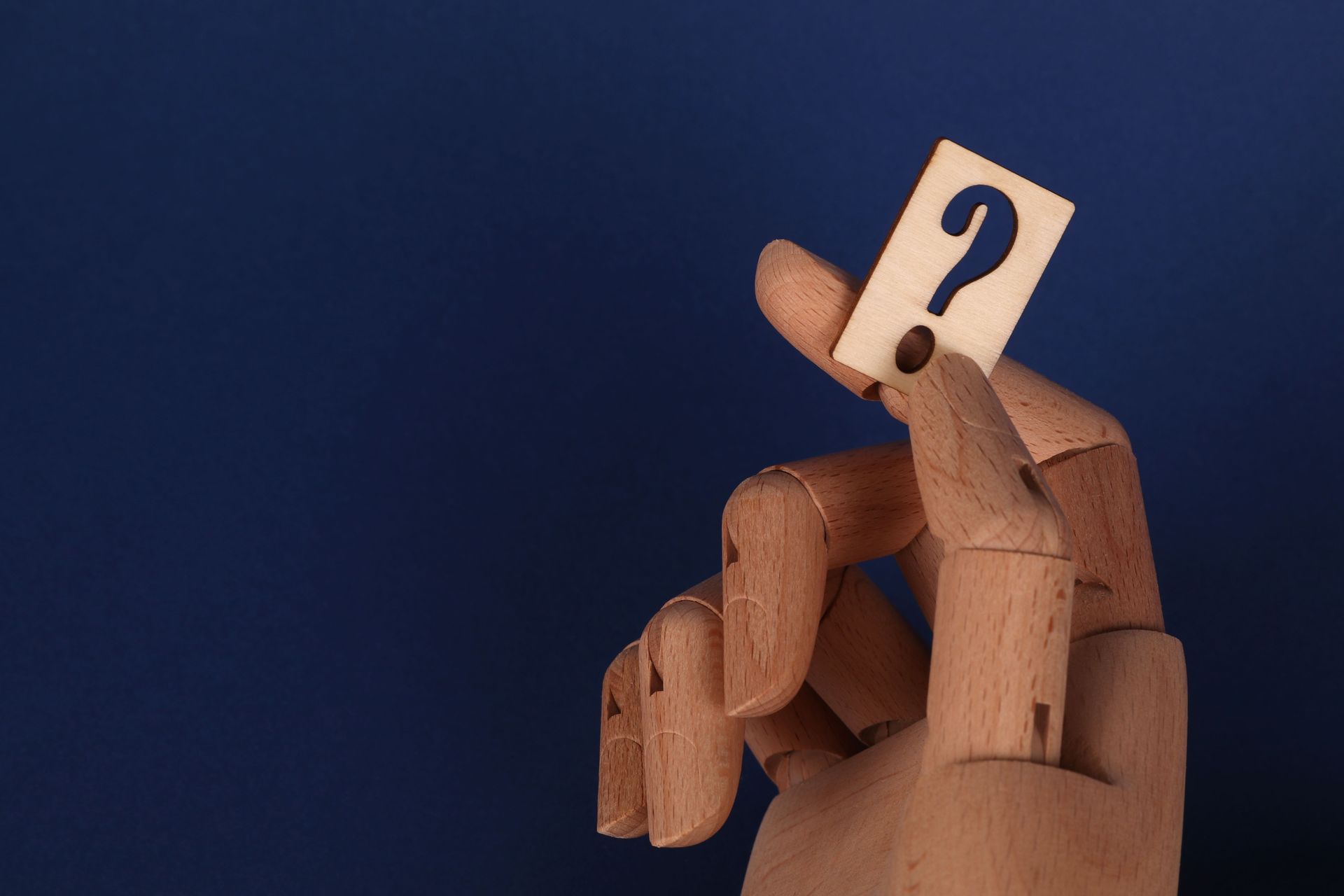 Wooden mannequin with a question mark above its head against a dark blue background