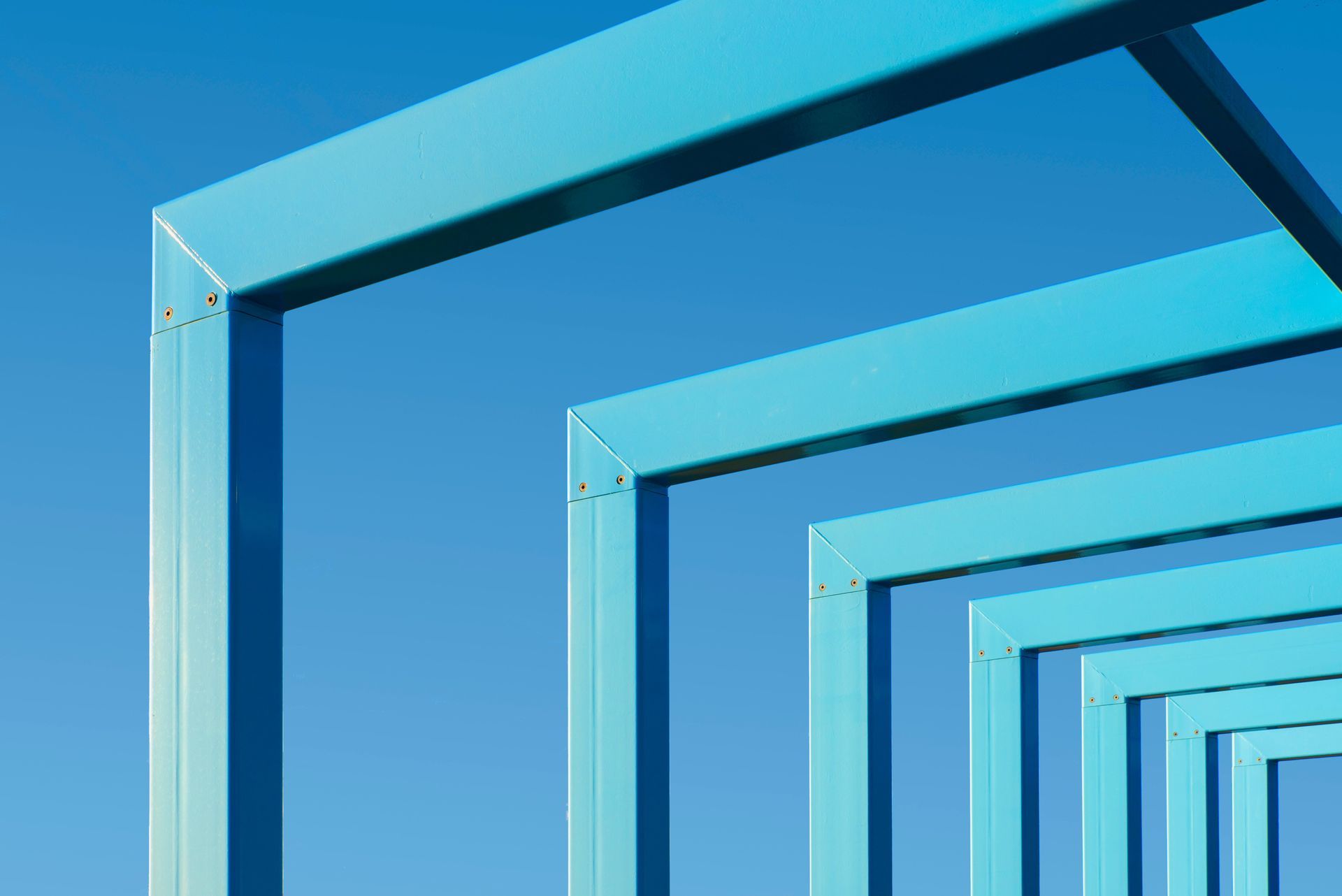Blue geometric metal frames receding into the distance against a clear sky