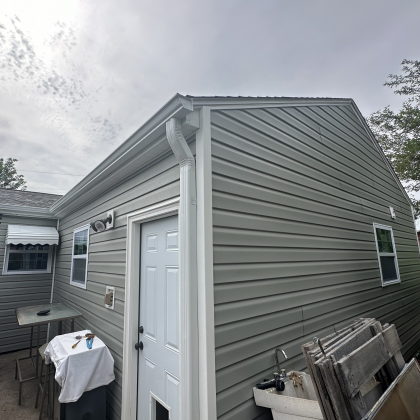 Exterior of a home with sage green horizontal siding, white trim, a white door, and a white gutter and downspout.