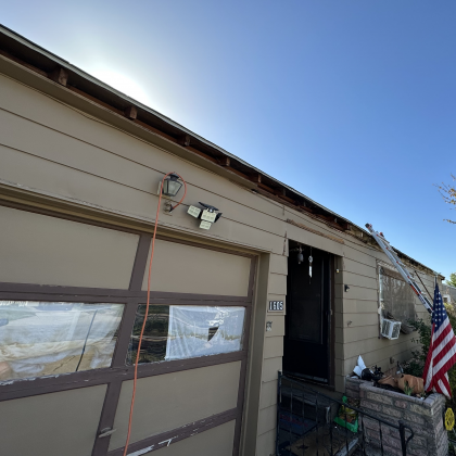 A tan house with a garage door, security lights, a covered entryway, and an American flag on the side.
