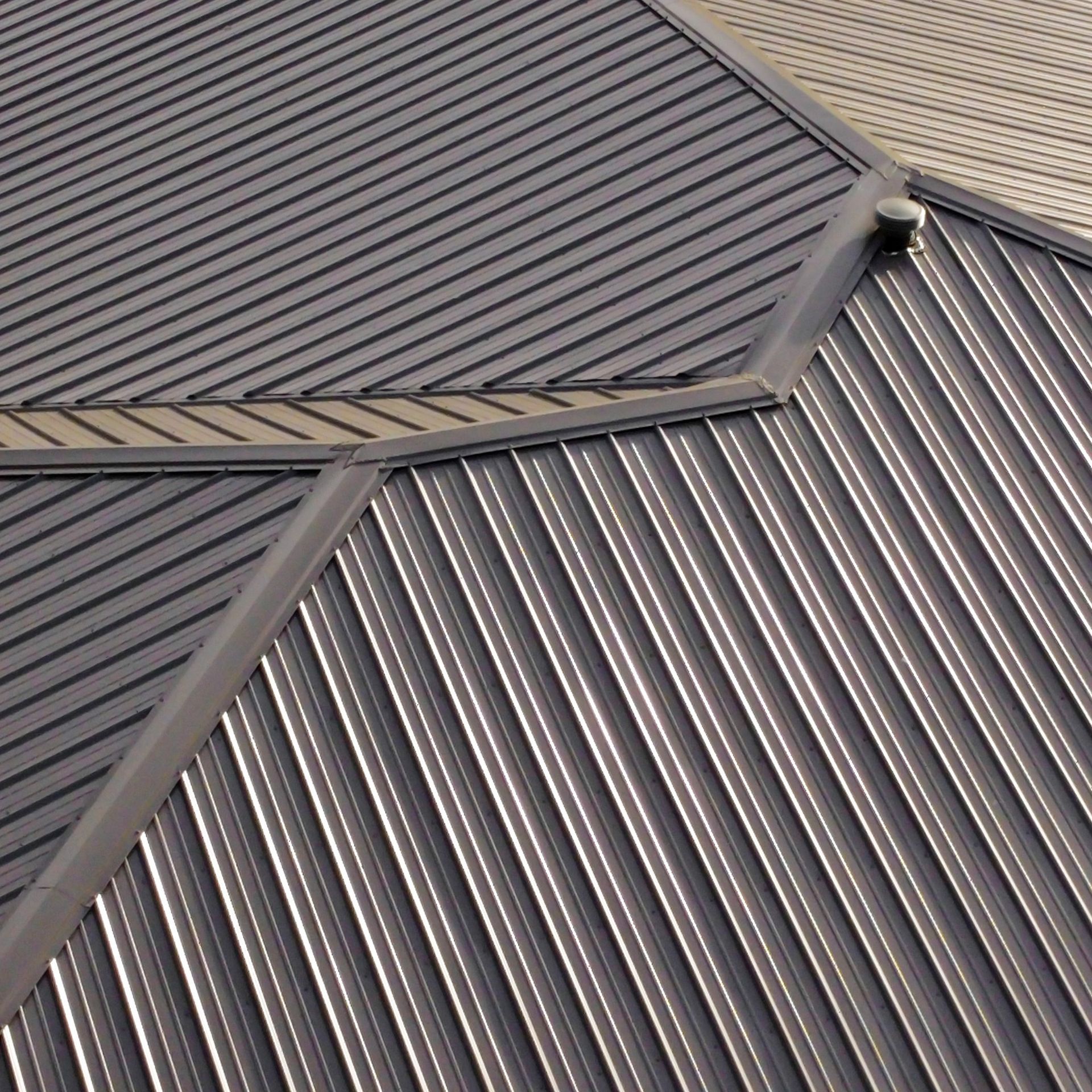 A close-up view of a metal roof with overlapping dark gray panels and angled drainage seams.