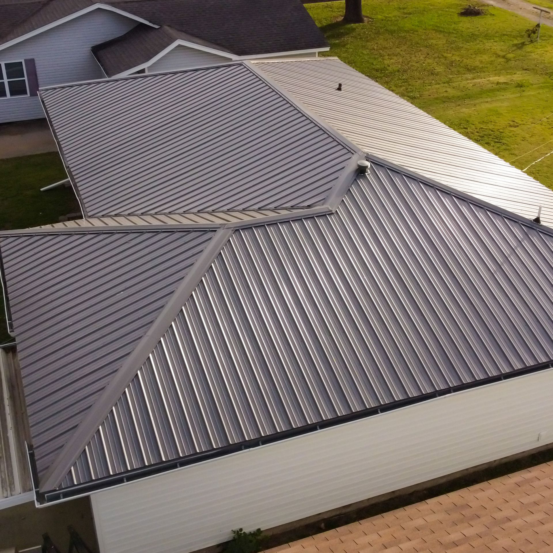 An aerial view of a dark grey standing seam metal roof on a residential home with white siding.
