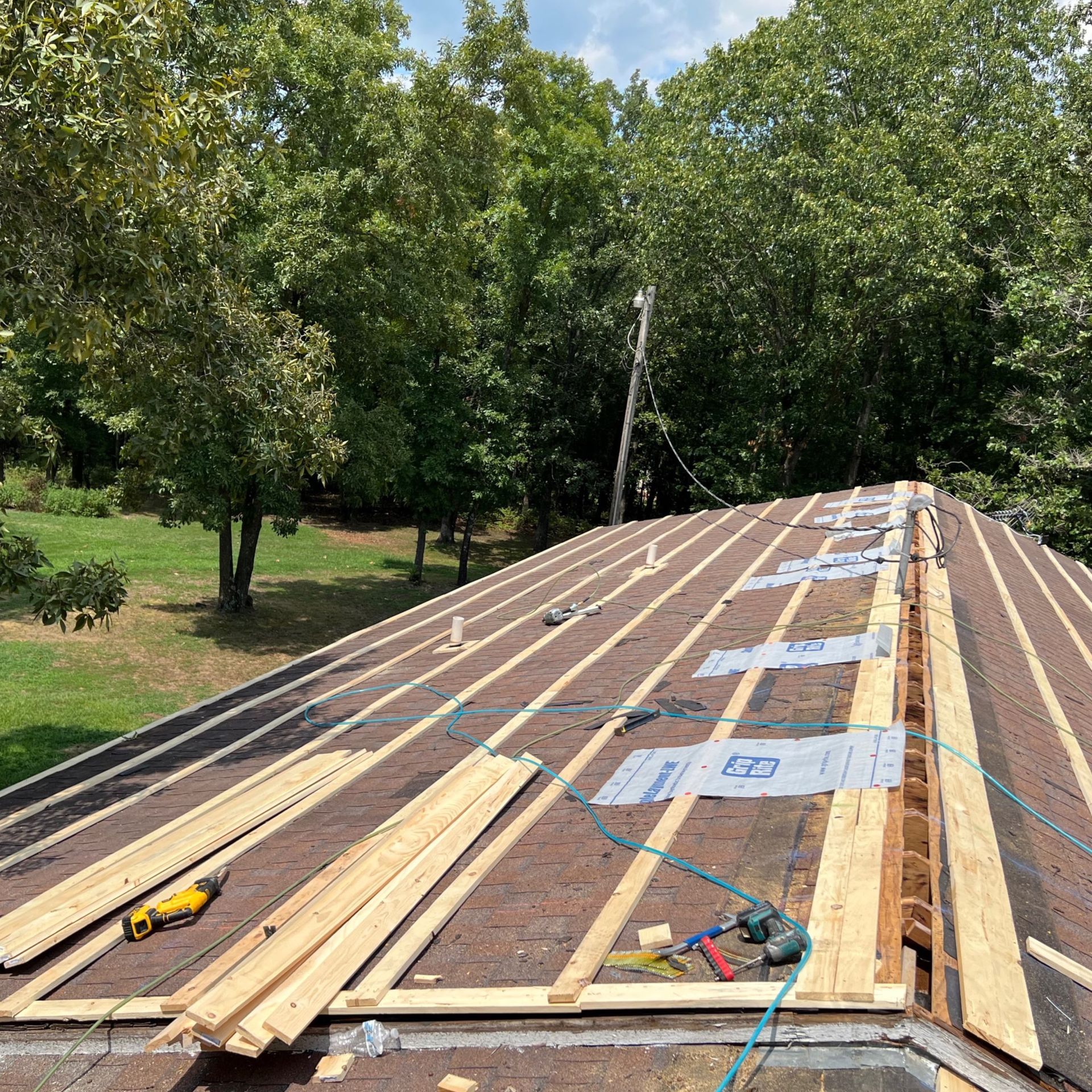 A view from above of a roof under construction with wooden furring strips laid over shingles and sections of underlayment.