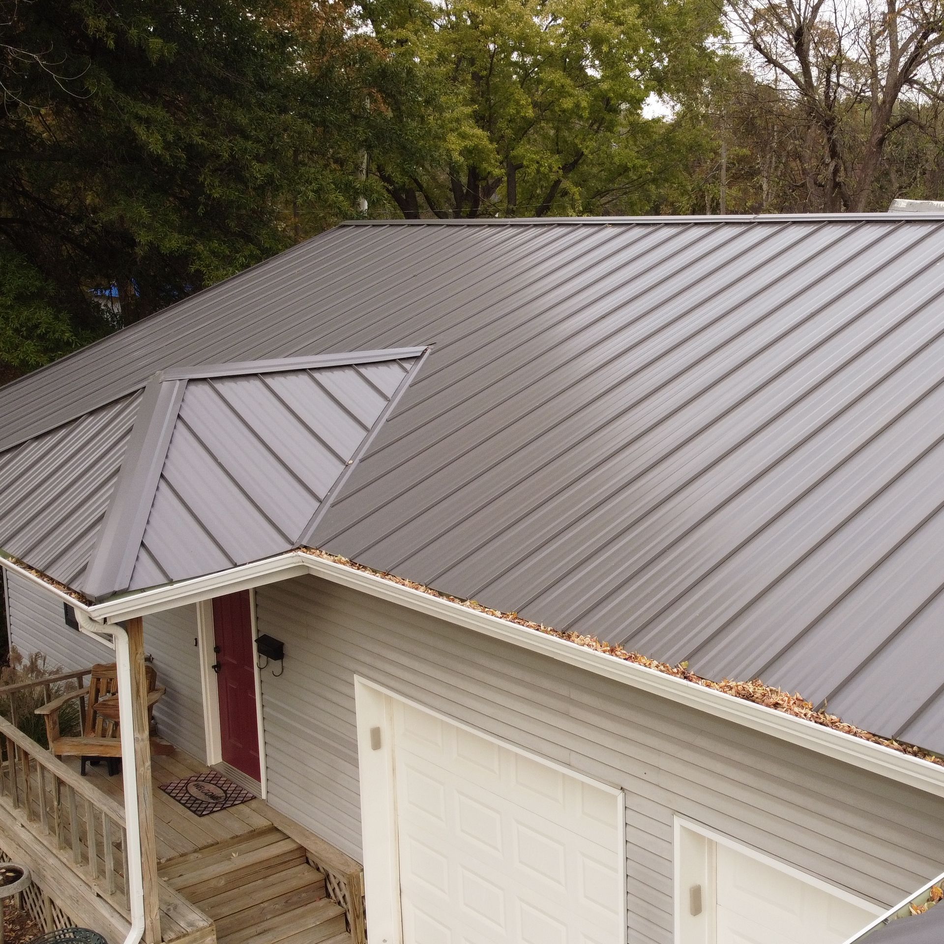An elevated view of a house with a gray standing-seam metal roof, a front porch, and a white garage.
