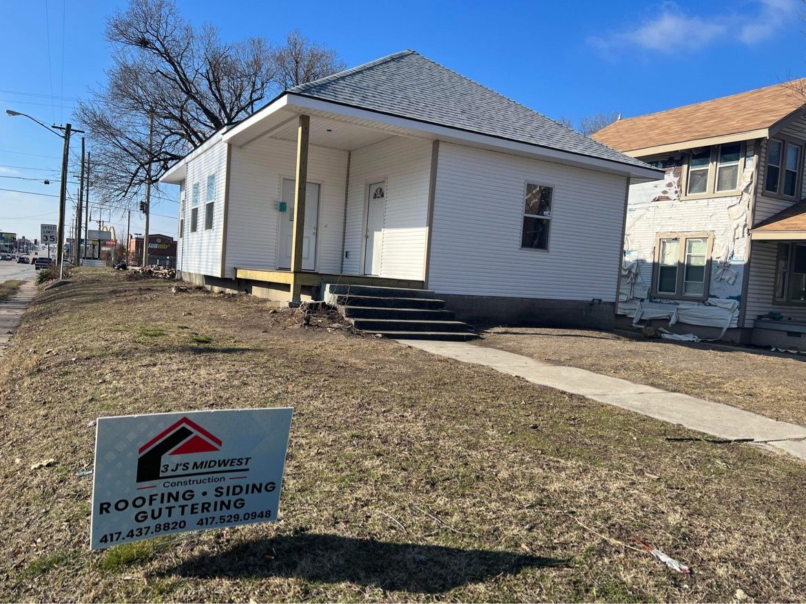 A white house with new siding stands near a yard sign advertising 