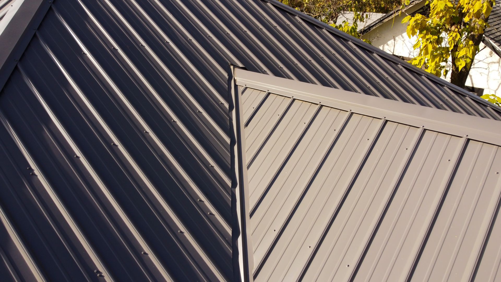 A close-up of a metal roof with dark grey diagonal panels meeting a light grey section at a roof valley.