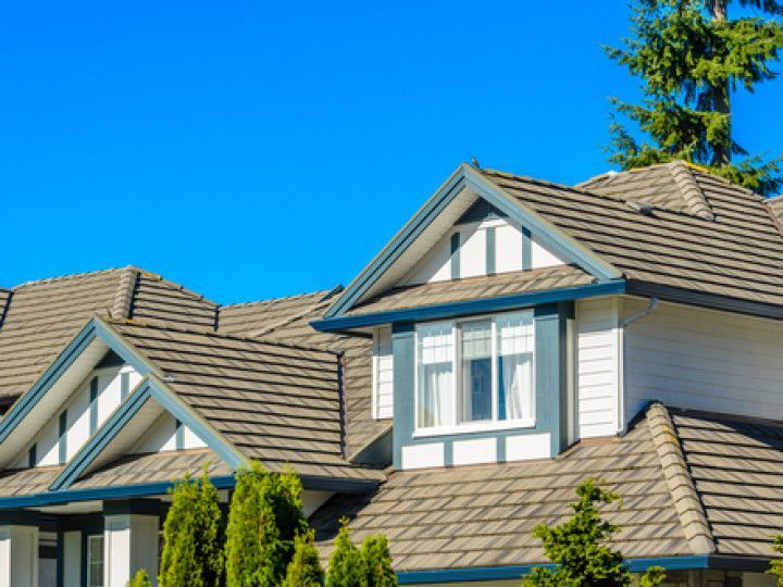 A close-up of a house roof featuring gray shingles, white gables, and dark blue trim against a clear blue sky.