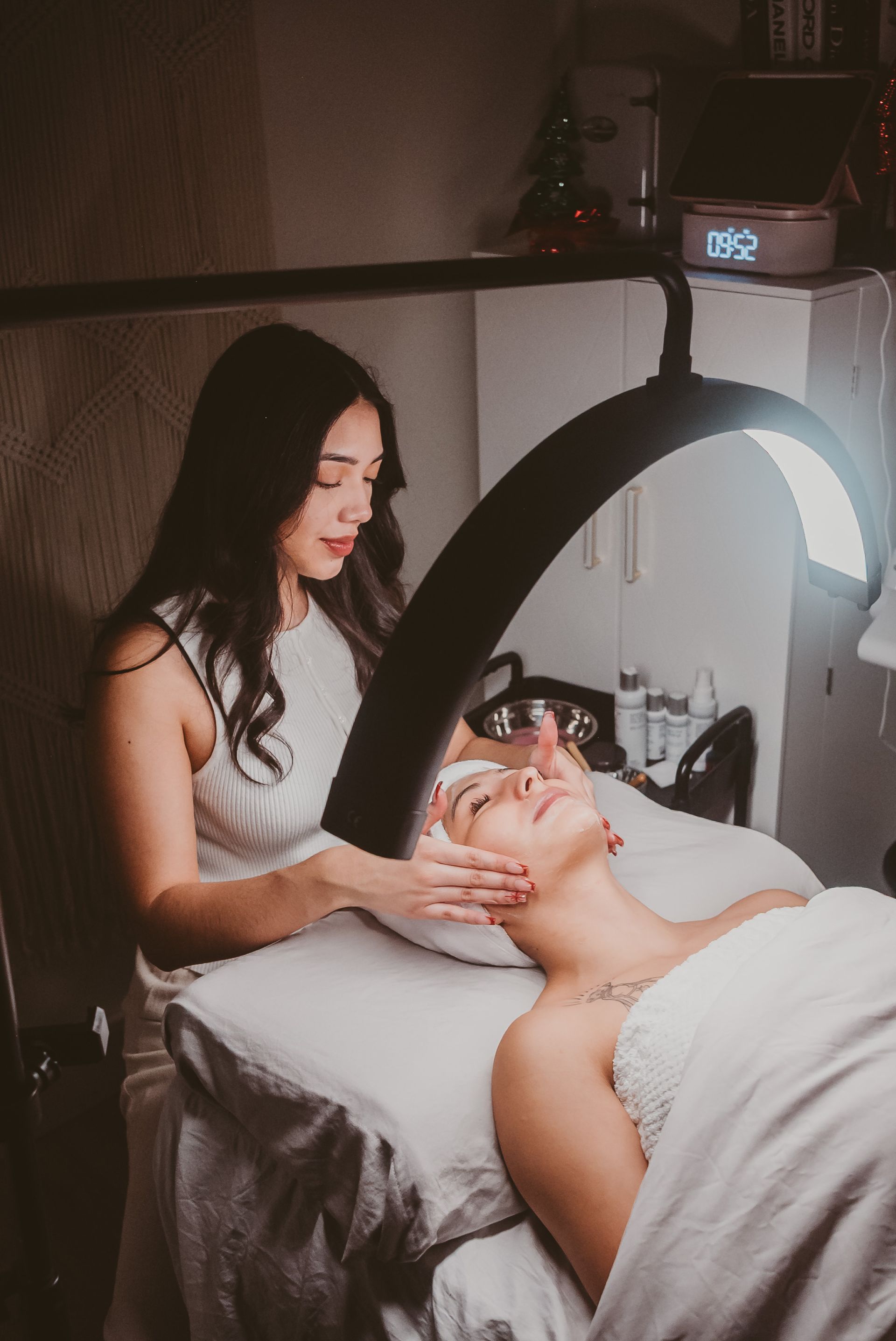 Woman in black shirt giving facial treatment to person lying down.