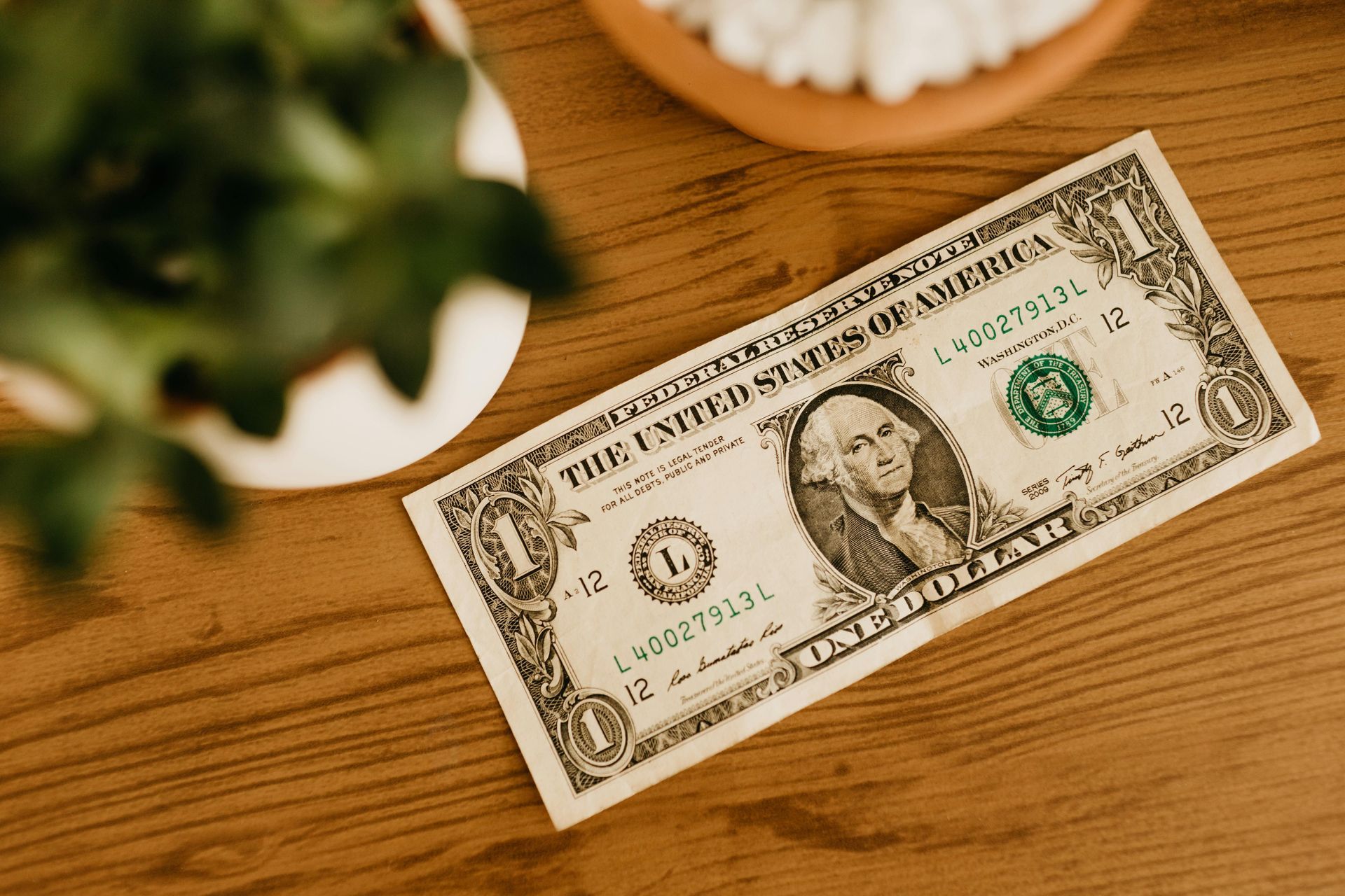 A dollar bill is sitting on a wooden table next to a plant.