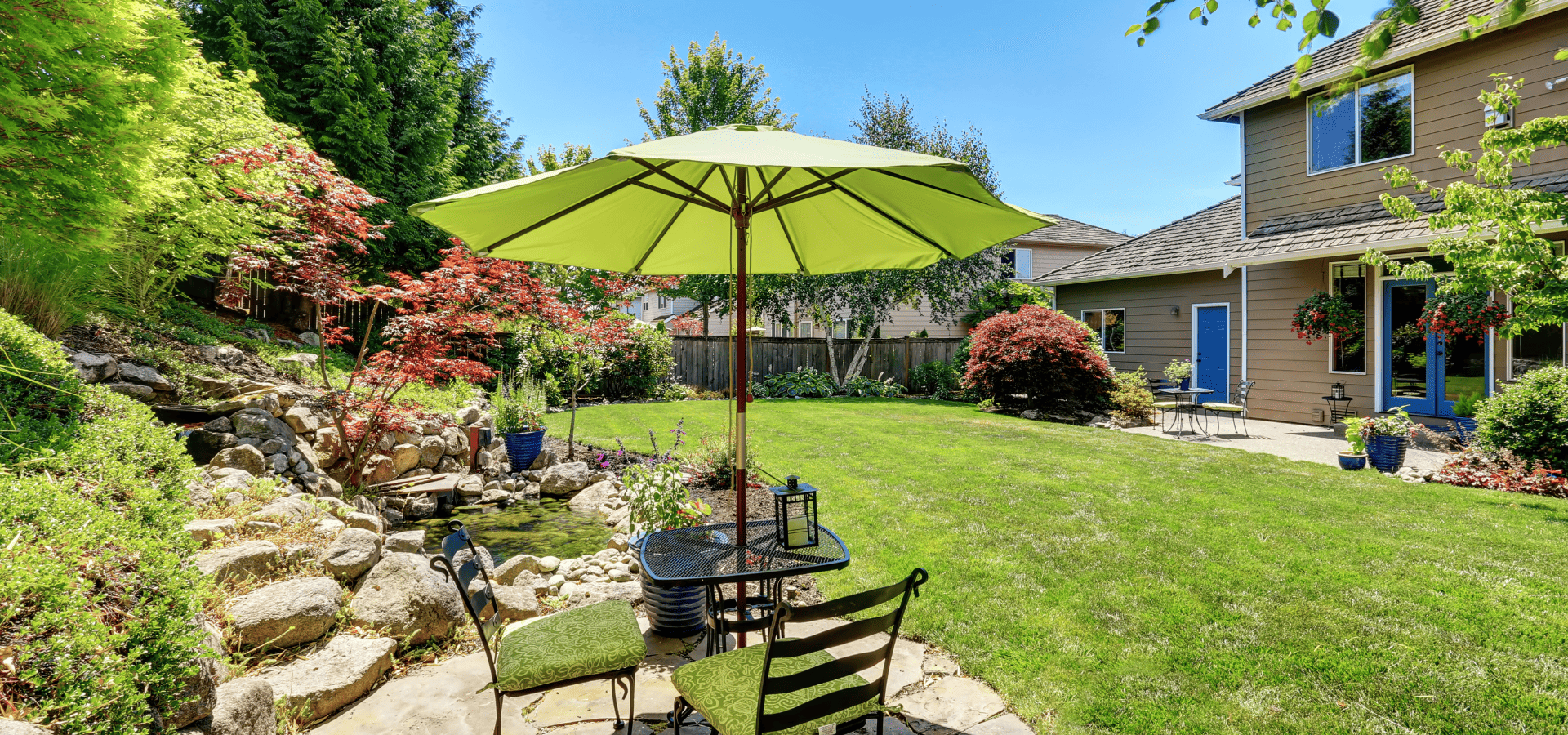 A backyard in summer with a patio table equipped with a built-in umbrella