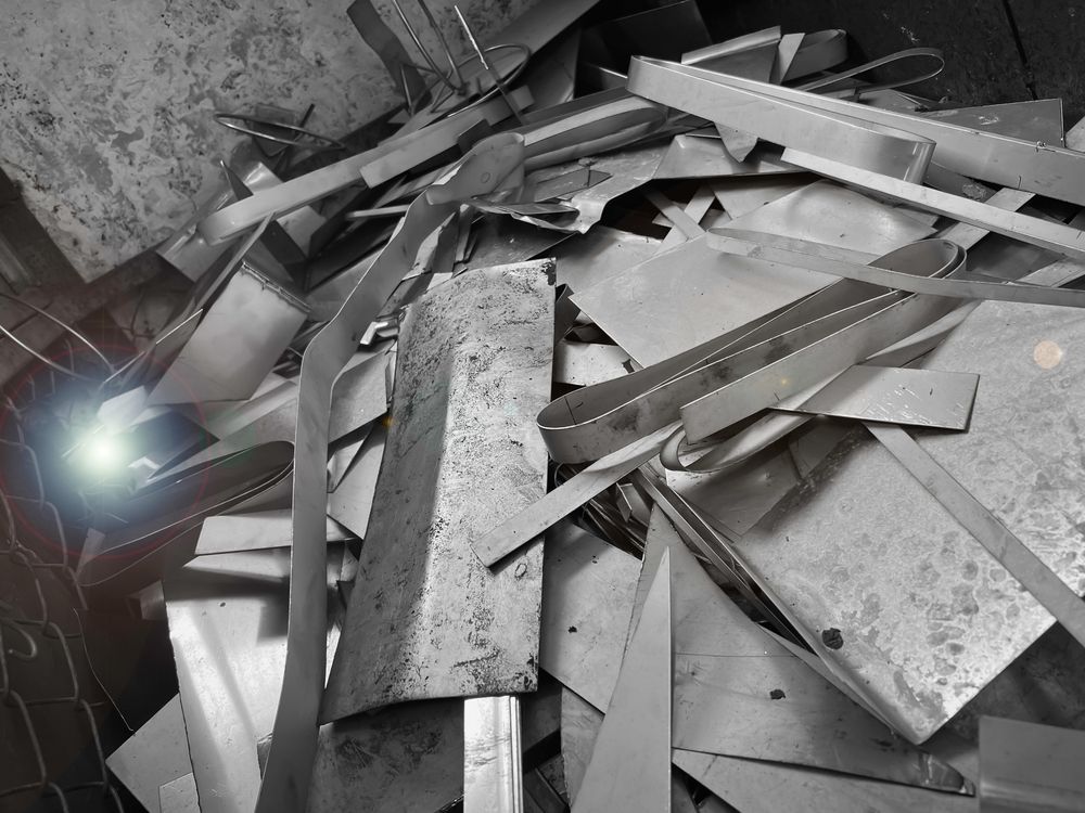Pile of broken metal scraps and panels on a concrete floor, lit by a bright light.