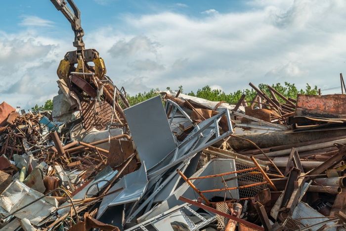 Excavator sorting a pile of demolished building debris under a partly cloudy sky