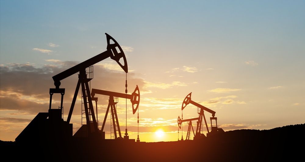 Oil pumpjacks silhouetted against a golden sunset sky.