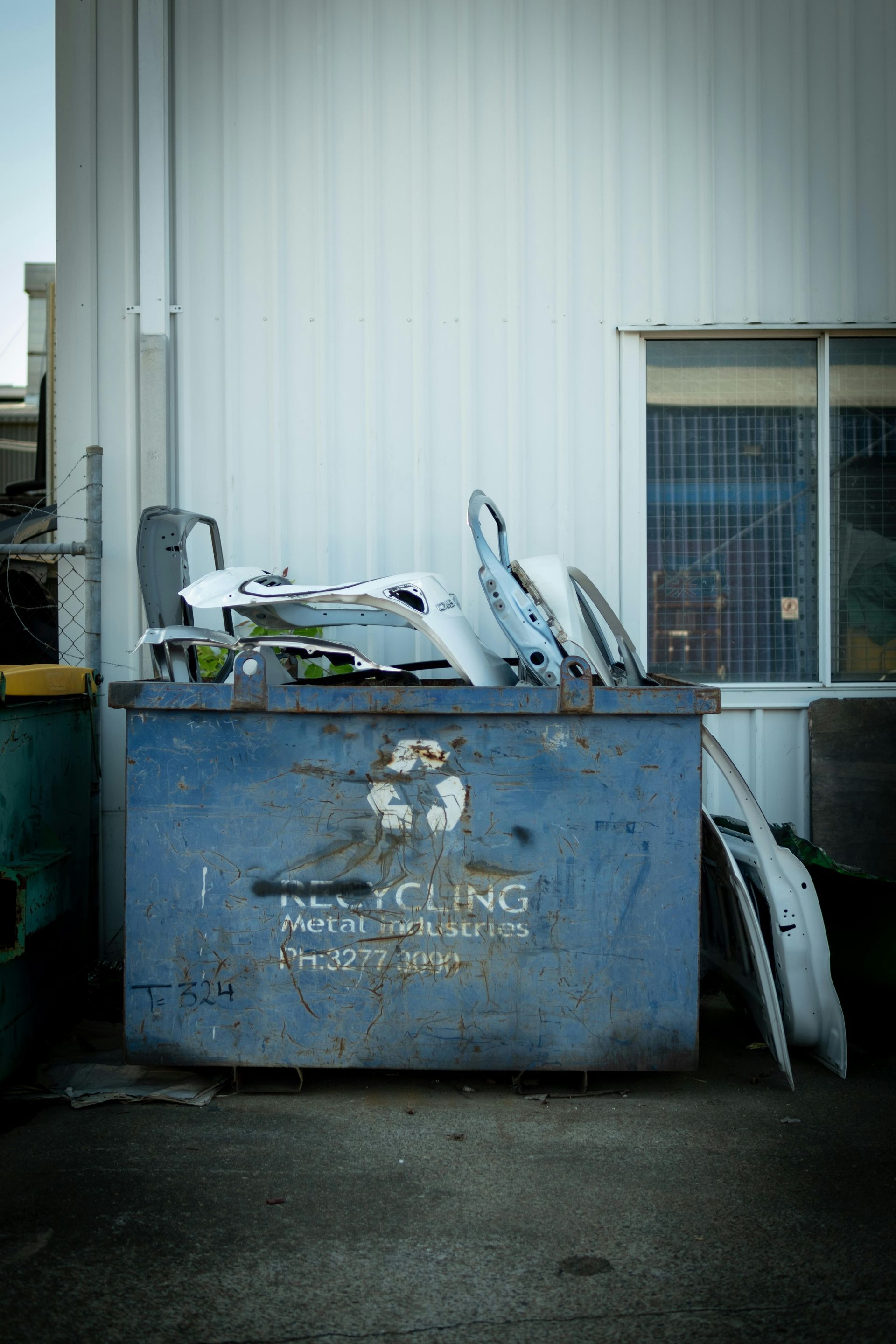 Blue dumpster full of discarded furniture against a white building wall